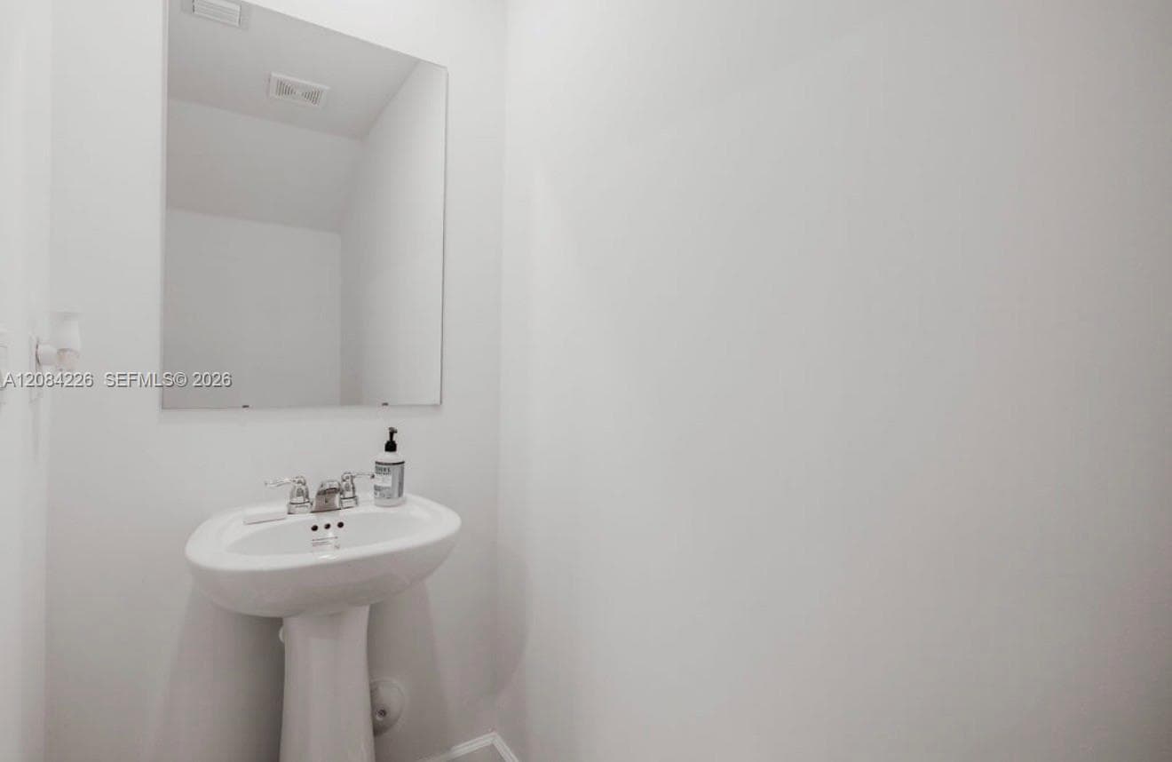 White pedestal sink with a polished chrome widespread faucet, frameless rectangular wall mirror, and neutral-toned wall paint