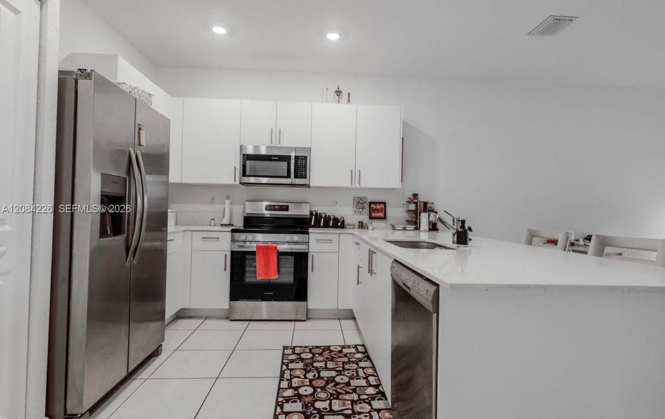 Kitchen featuring white flat-panel cabinetry, light-toned countertops, tile flooring, and a stainless steel appliance suite including a built-in microwave and dishwasher