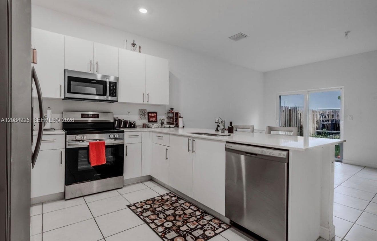Kitchen featuring white cabinetry, stainless steel appliances, stone-surface countertops, a breakfast bar, and tile flooring