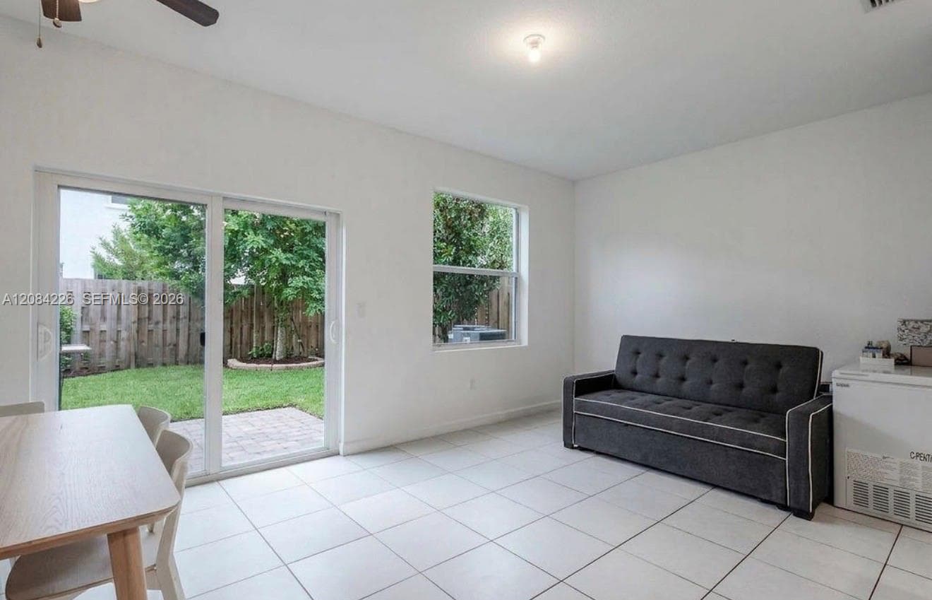 Neutral-tone tile flooring, sliding glass door, single-pane window, ceiling fan, and access to a paved patio