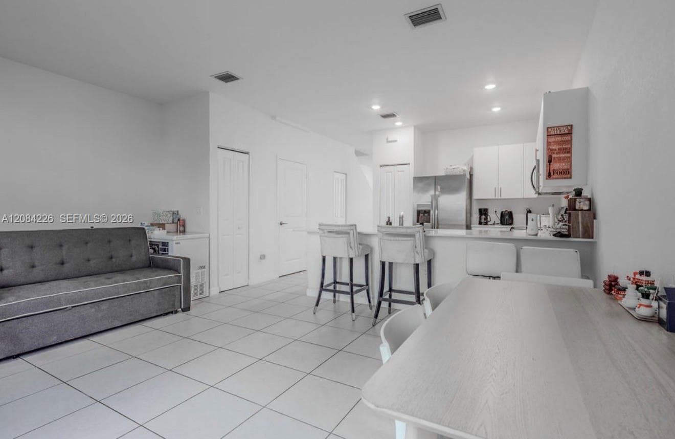 Open-concept interior featuring large-format ceramic tile flooring, white cabinetry, stainless steel kitchen appliances, and a breakfast bar