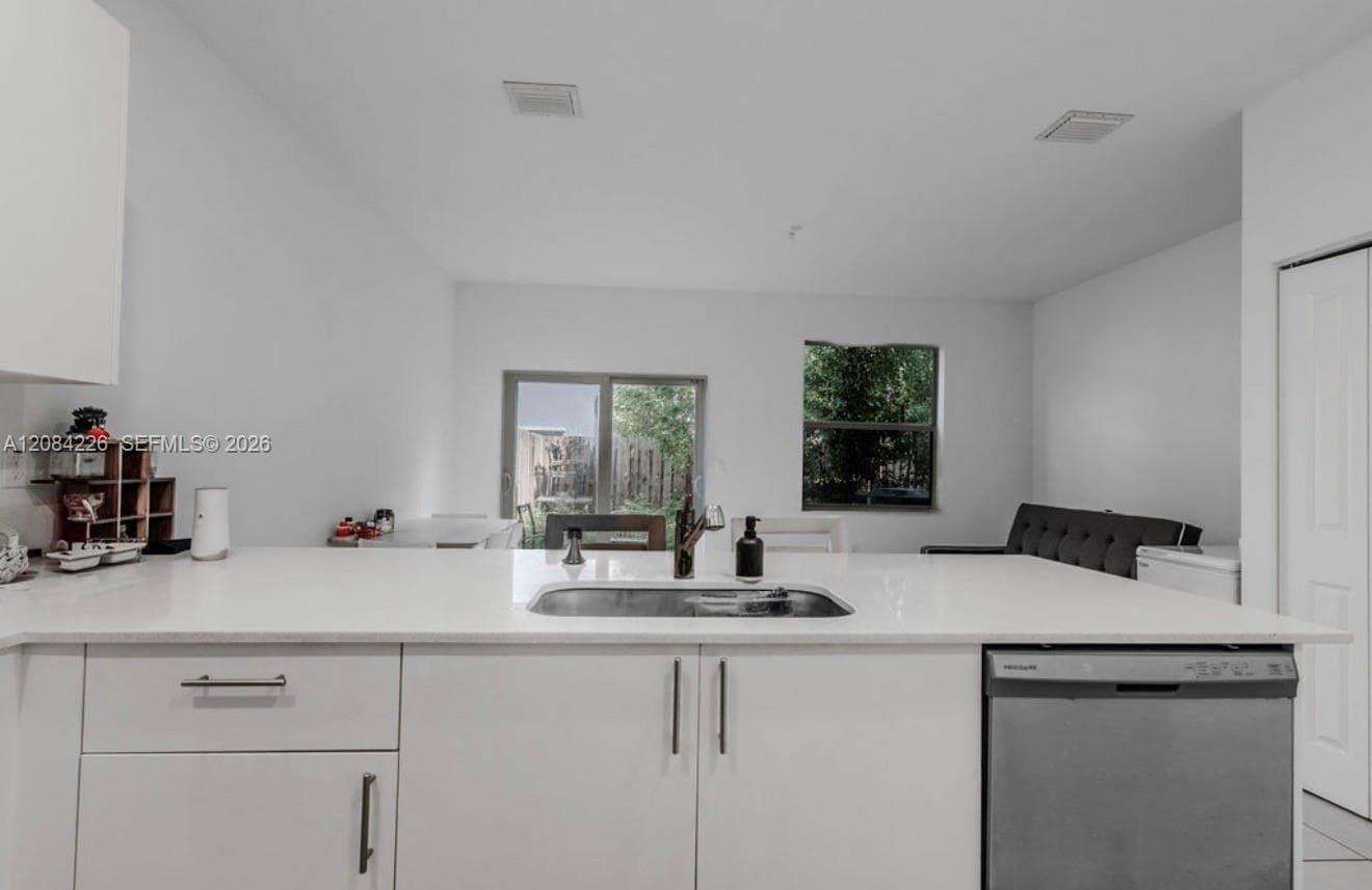 Kitchen featuring white flat-panel cabinetry, quartz countertops, a stainless steel undermount sink with a gooseneck faucet, and a stainless steel built-in dishwasher