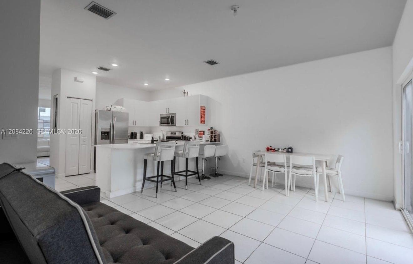 Open-concept kitchen featuring white cabinetry, a breakfast bar, recessed lighting, and tile flooring