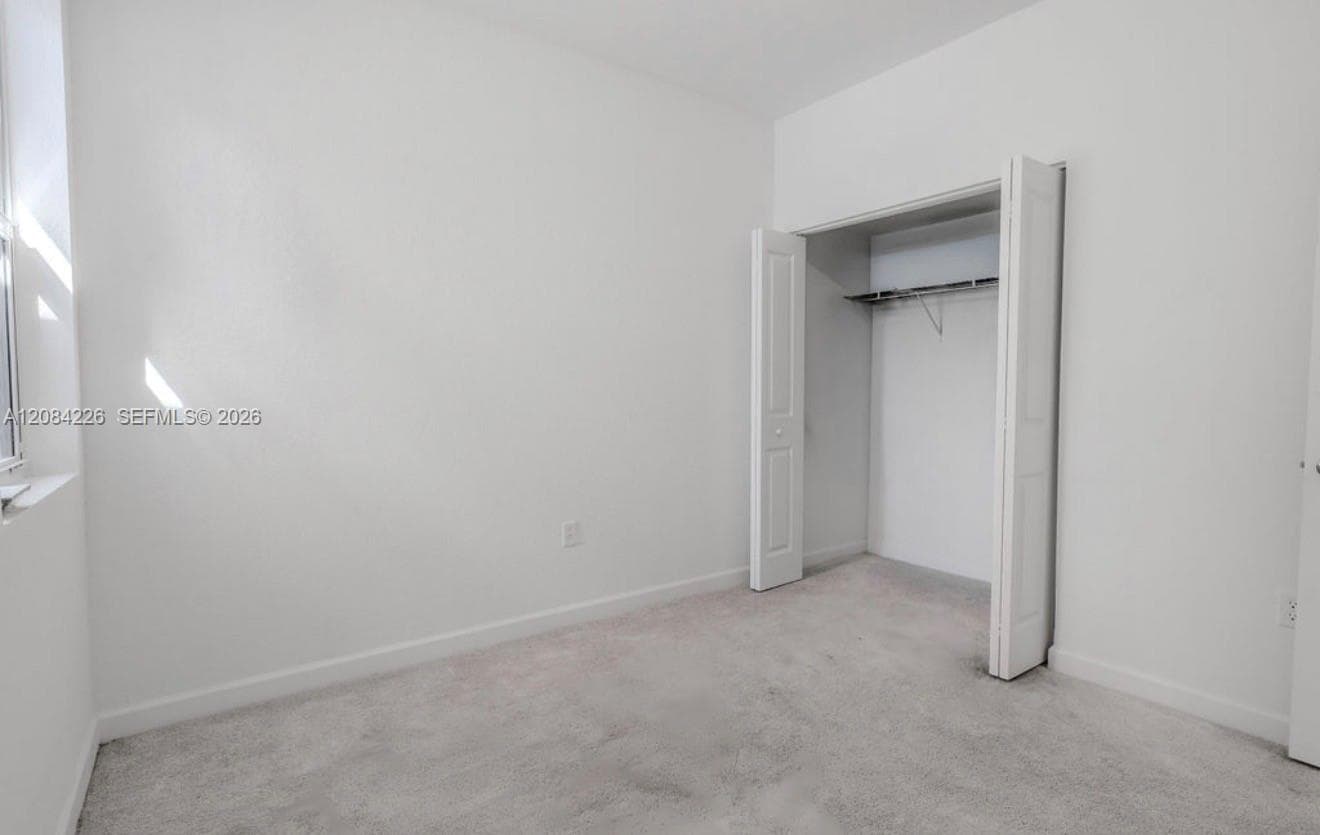 Neutral-toned carpeting, crisp white walls, and a reach-in closet featuring dual hinged doors and an integrated shelving rod
