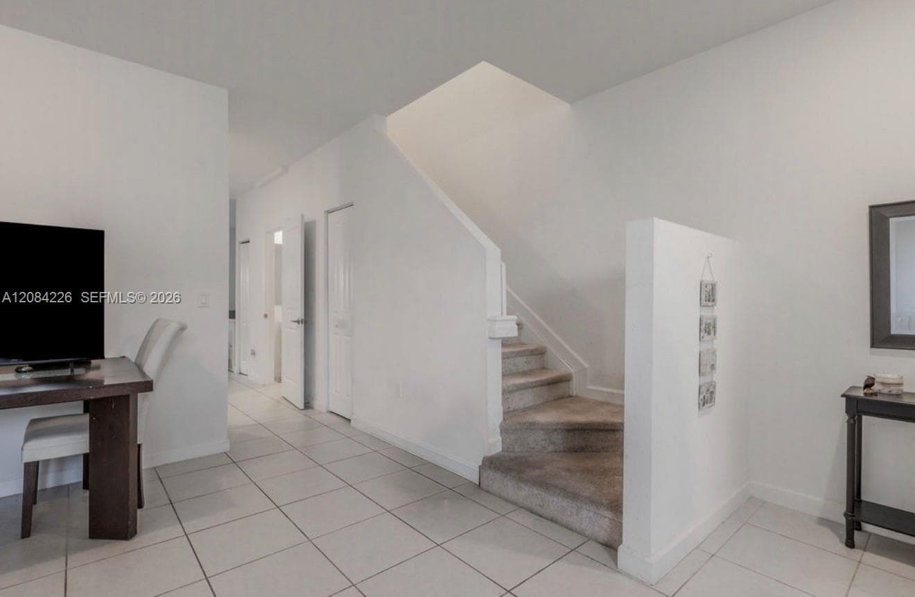 Interior space featuring neutral tile flooring, a half-wall partition, and a staircase with carpeted treads