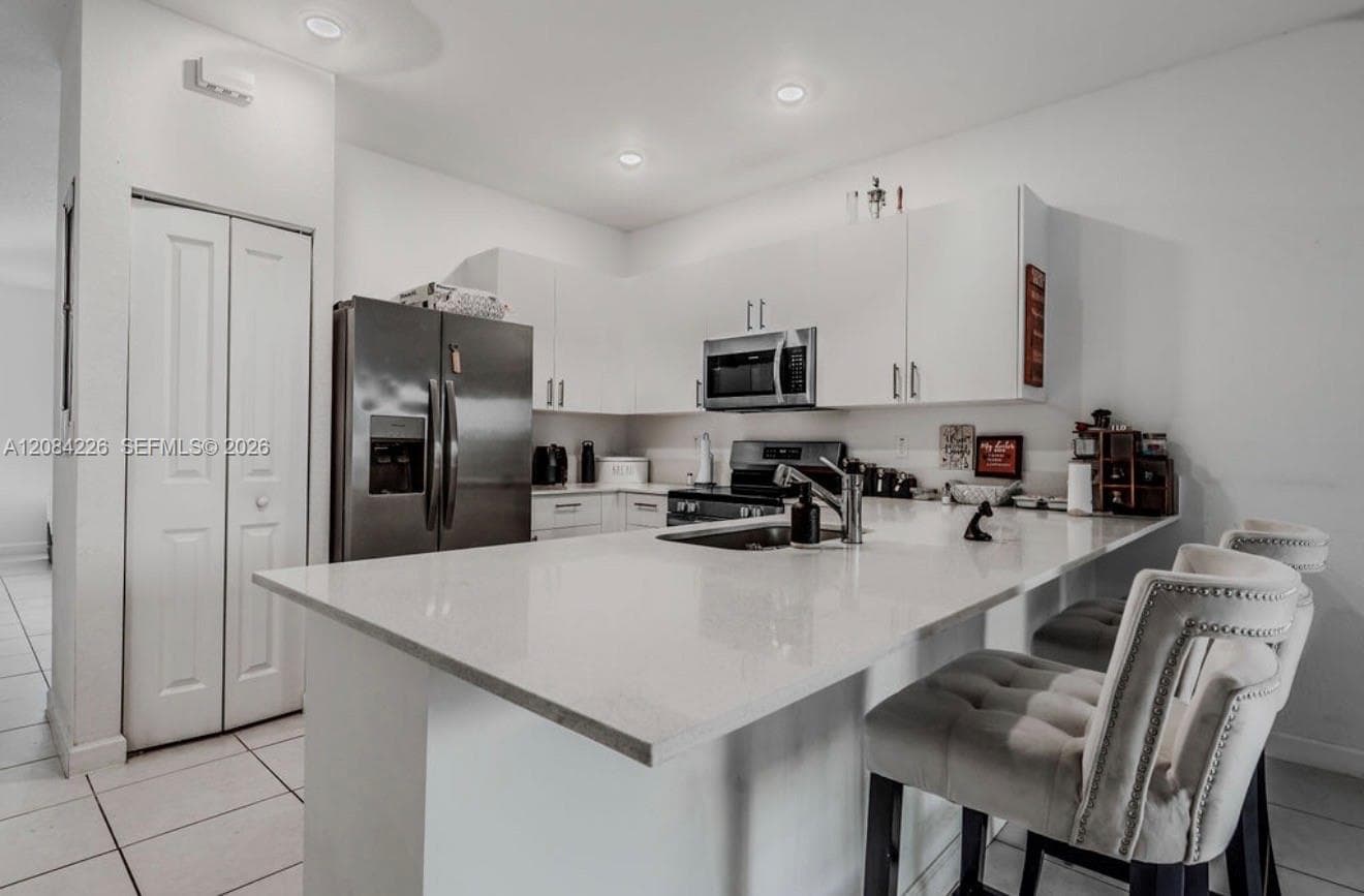 Kitchen featuring white flat-panel cabinetry, light-toned stone-surface countertops, an integrated island, stainless steel appliances, and tile flooring