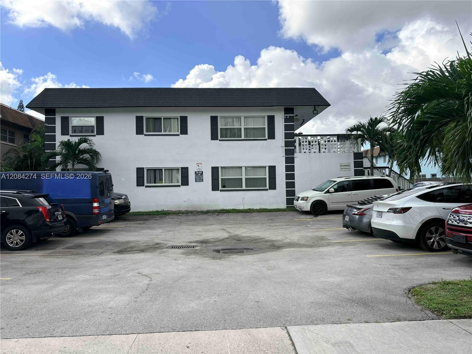 Two-story building featuring white stucco exterior, dark shutters, and a dark shingle roof