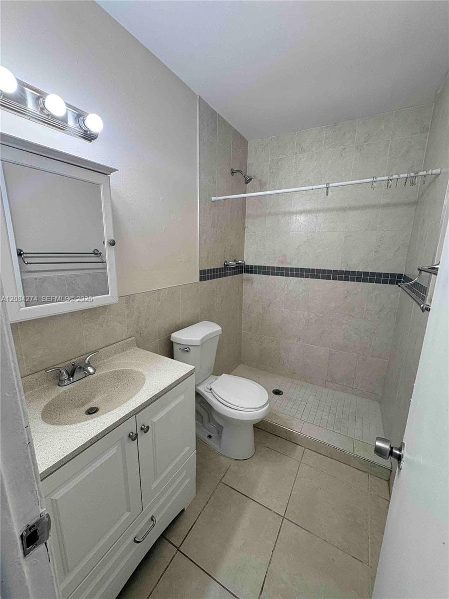 Vanity with integrated sink, chrome faucet, medicine cabinet with mirror, tiled shower enclosure with dark accent border, and ceramic floor tiling