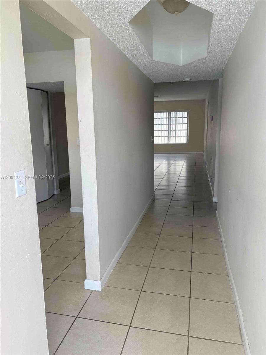 Neutral-toned tile flooring, recessed ceiling light fixture, textured ceiling, light-colored wall paint