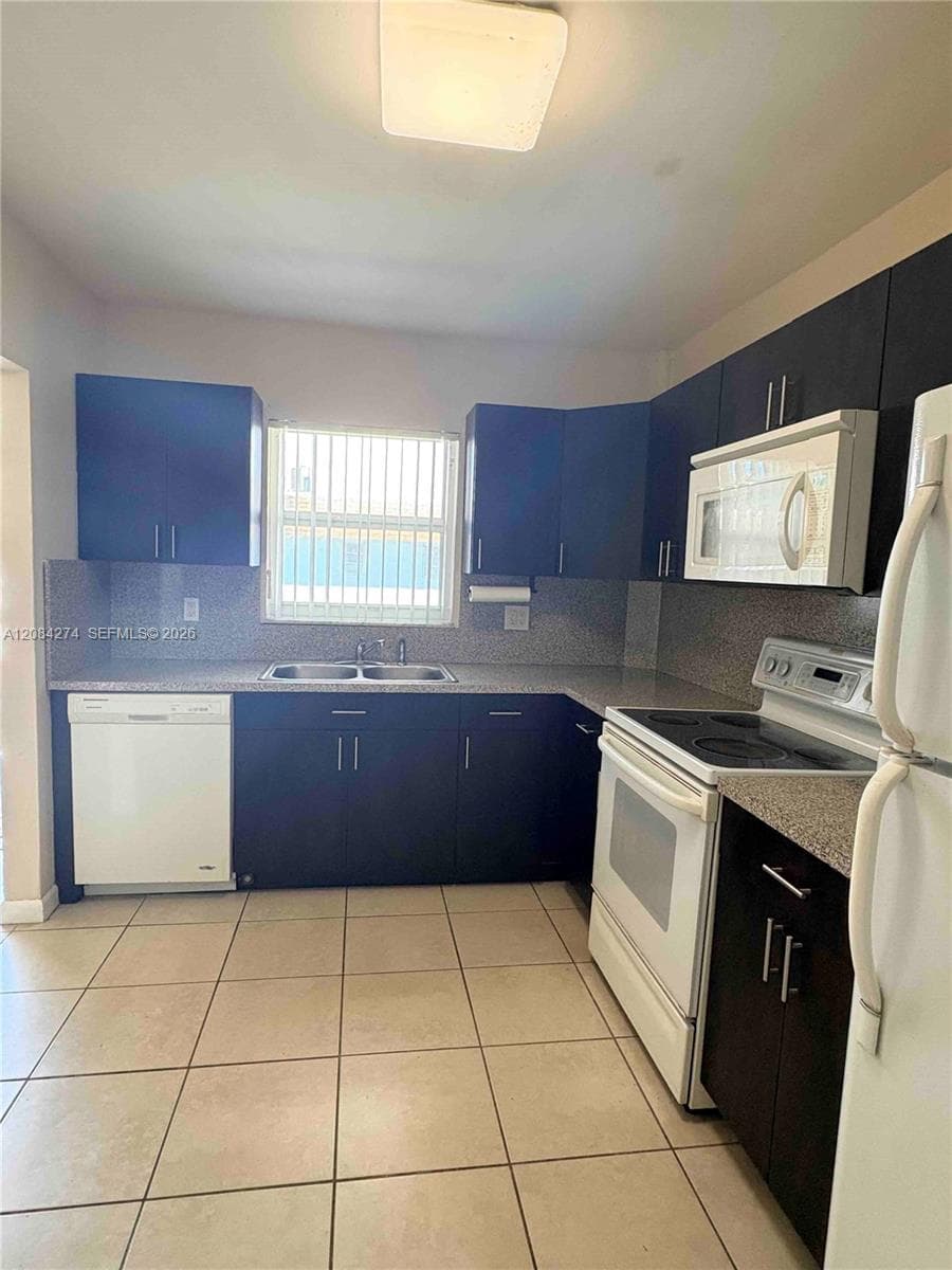 Kitchen featuring dark wood-finish cabinetry, solid surface countertops, a double basin sink, and tile flooring