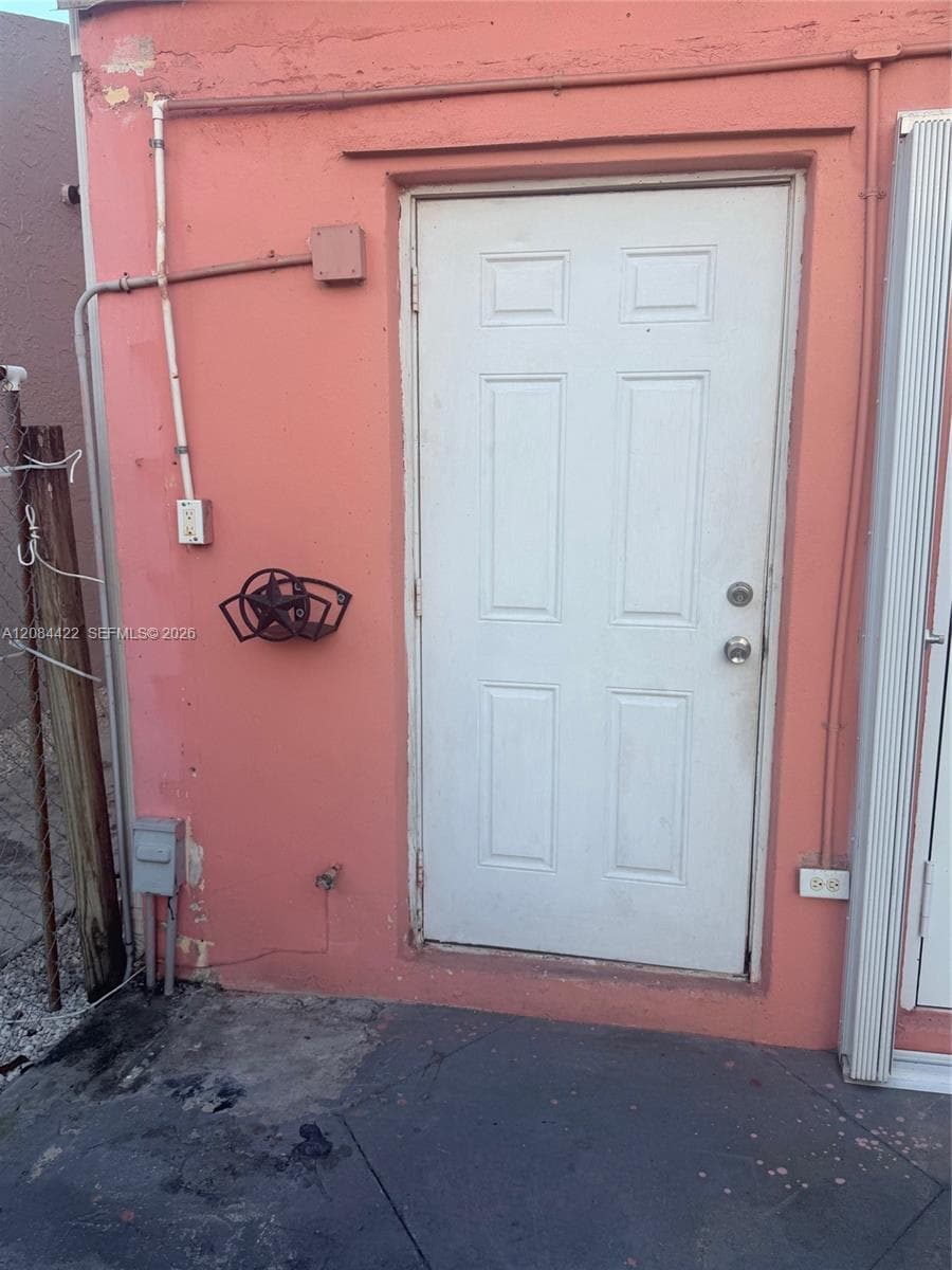 Exterior entrance featuring a six-panel white door, smooth stucco finish, and exterior electrical fixtures