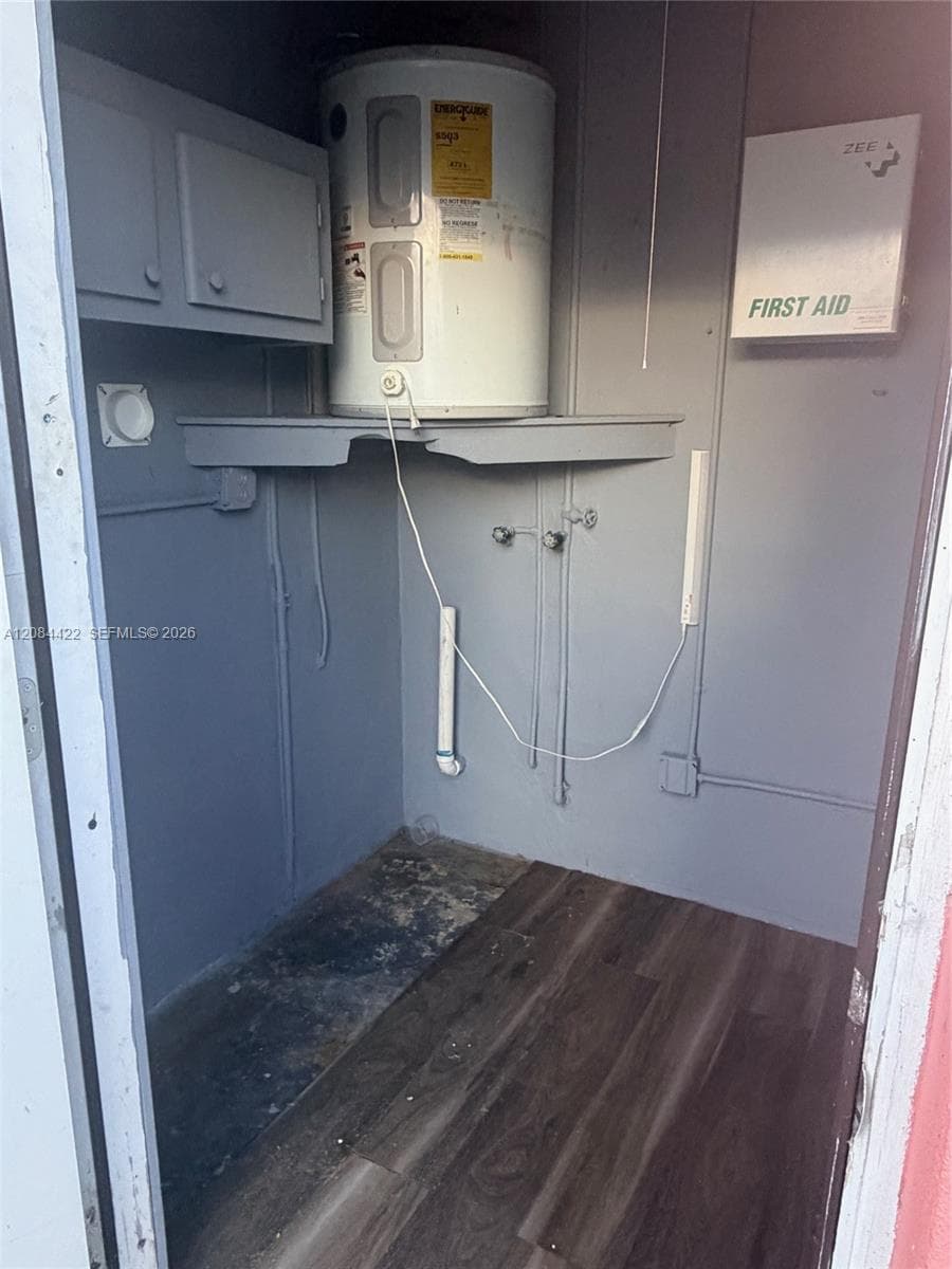 Utility space featuring wood-finish flooring, wall-mounted water heater with integrated shelving, and overhead cabinetry