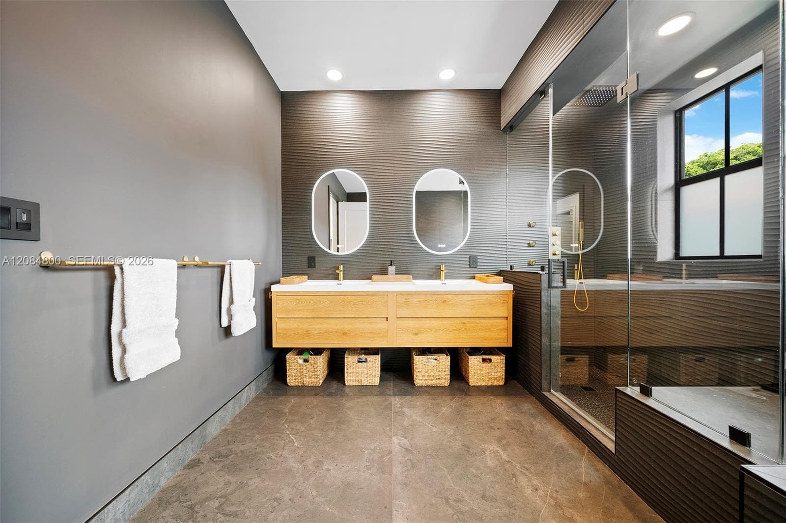Dual-sink floating vanity with backlit mirrors and brass fixtures in the spa-like primary bath