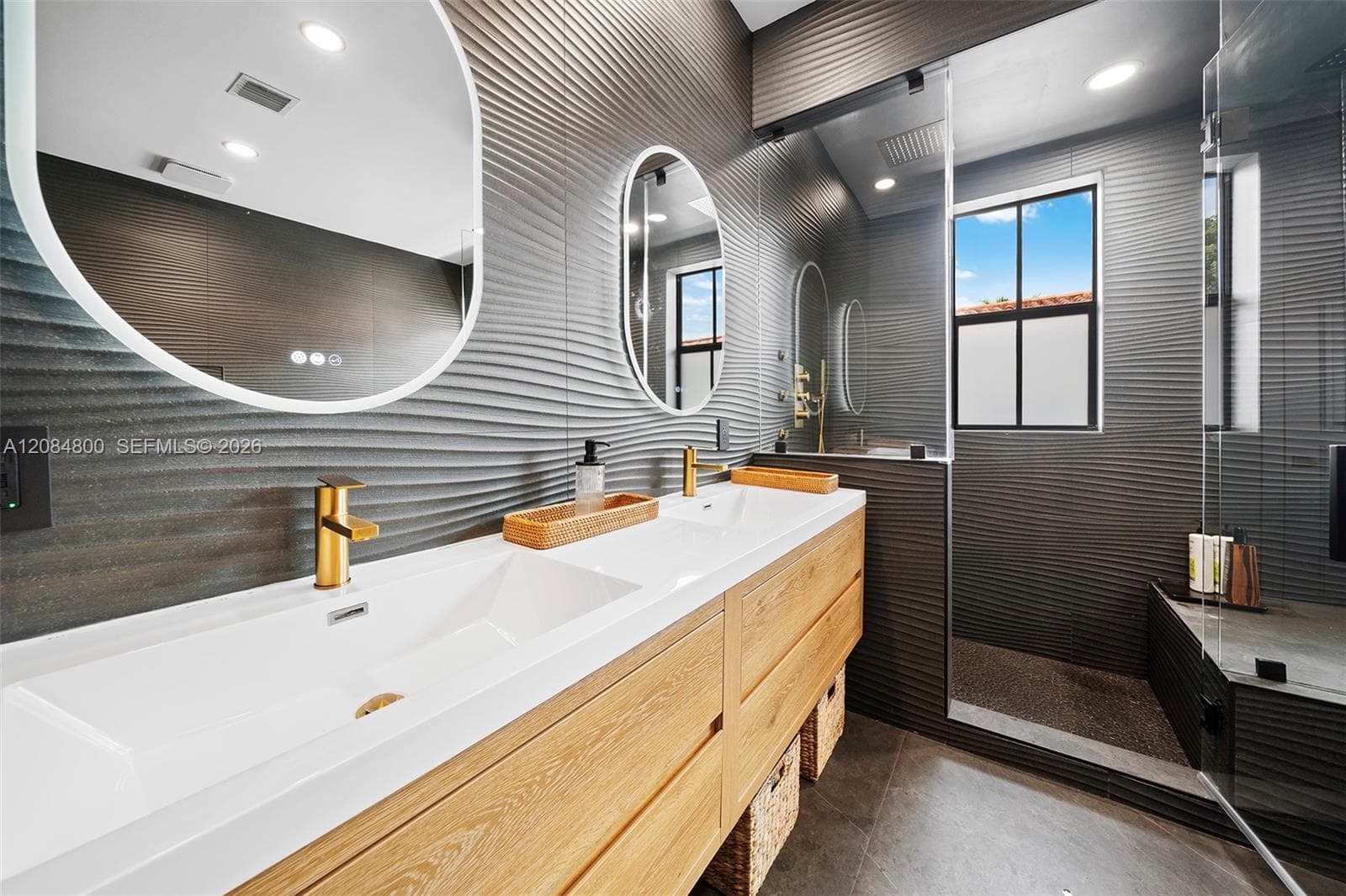 Sculpted wave tile, brushed brass fixtures, backlit mirrors — impeccable