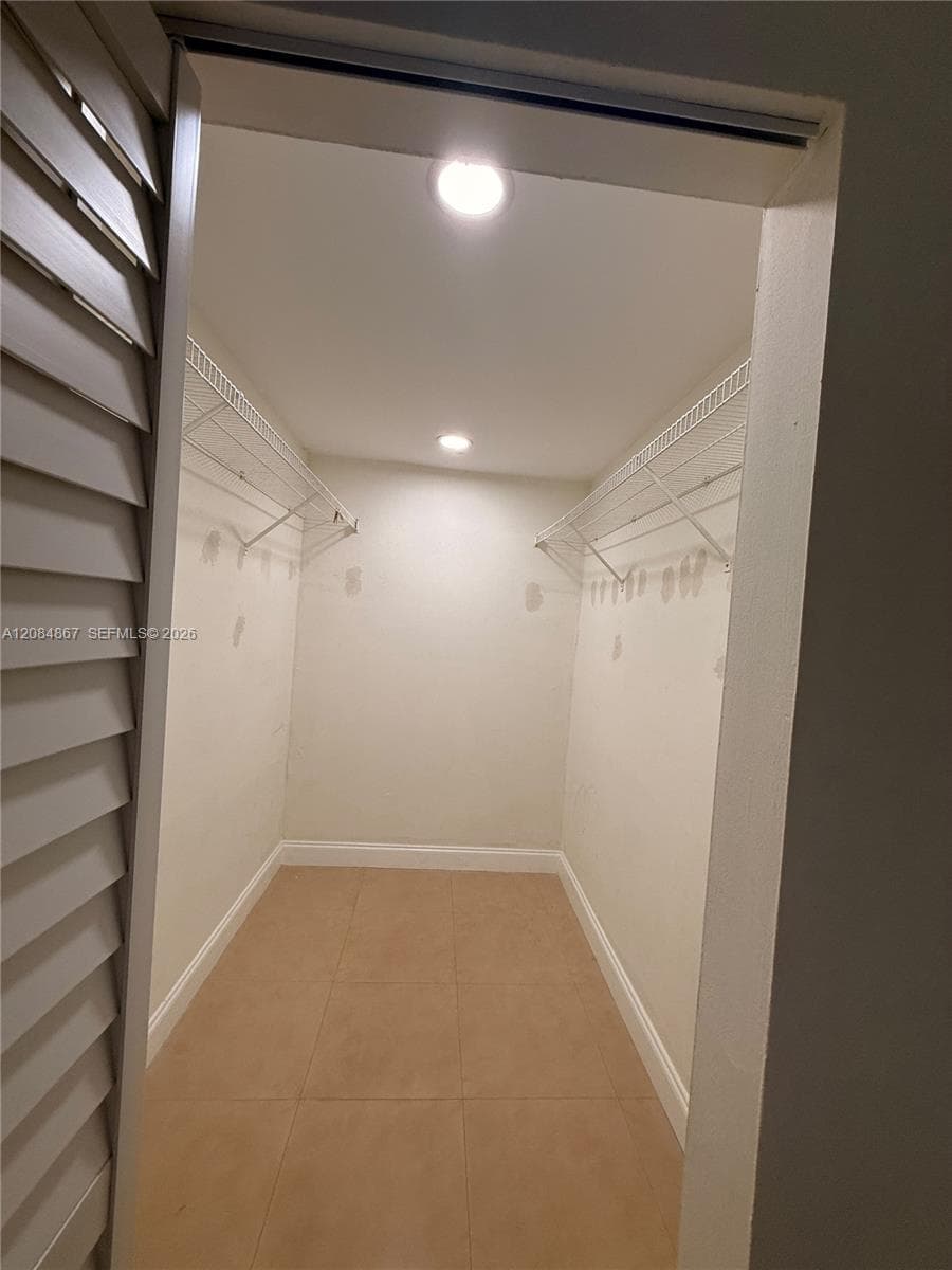 Walk-in closet featuring ceramic tile flooring, dual wire shelving units, recessed ceiling lighting, and louvered folding doors