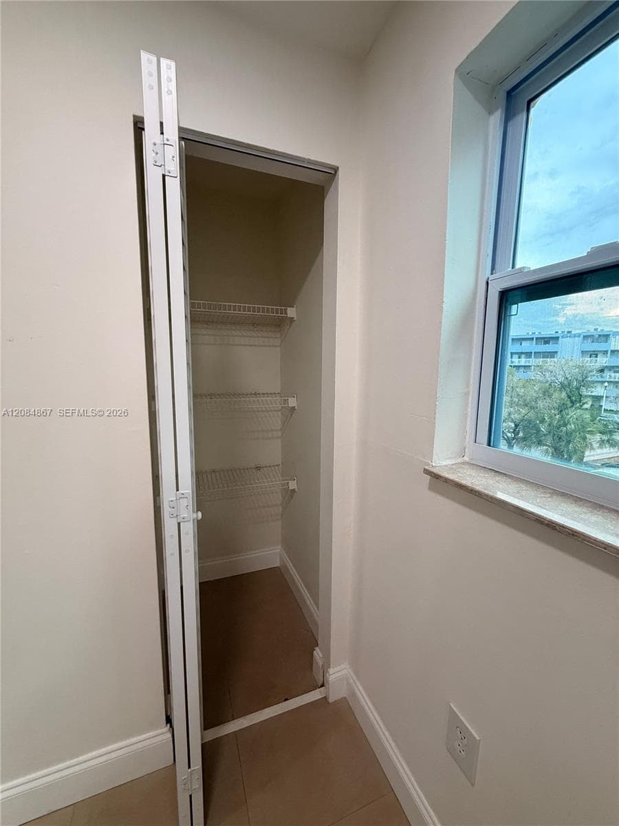 Storage closet with white wire shelving, bi-fold door, stone-finished windowsill, and neutral flooring