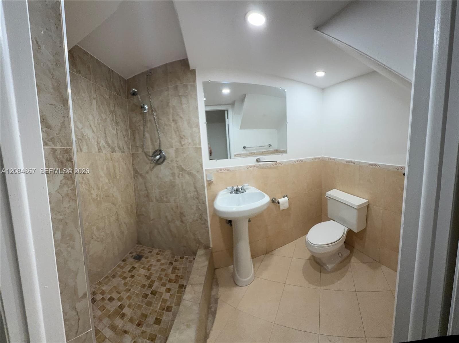 Bathroom featuring a walk-in shower with stone-tile surround, pedestal sink, wall-mounted mirror, and tile flooring