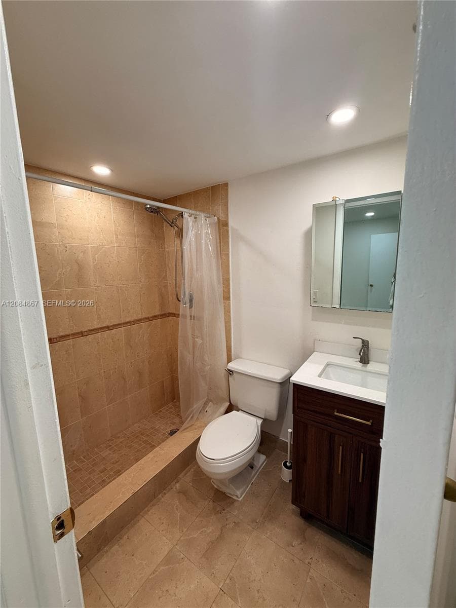 Bathroom featuring a dark wood-finish vanity, white countertop with integrated sink, wall-mounted medicine cabinet, recessed lighting, and a walk-in shower with tile surround