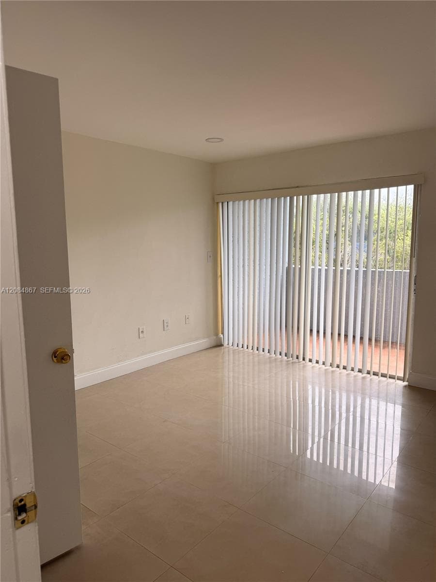 Interior space featuring large-format ceramic tile flooring, neutral wall tones, and glass sliding doors leading to an outdoor balcony