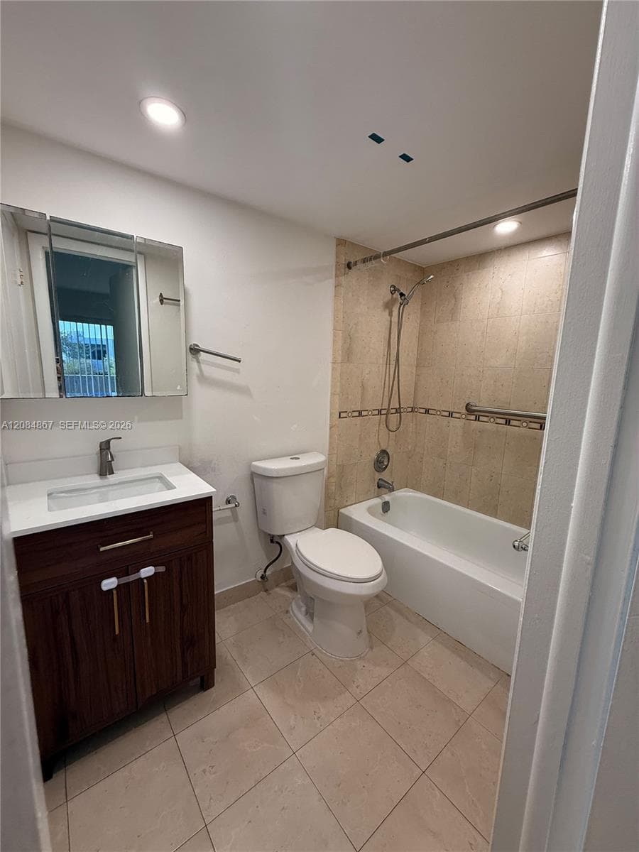 Bathroom featuring a dark wood-finish vanity with a white countertop, an integrated rectangular sink, a mirrored medicine cabinet, a tiled shower surround with an adjustable handheld showerhead, and neutral tile flooring