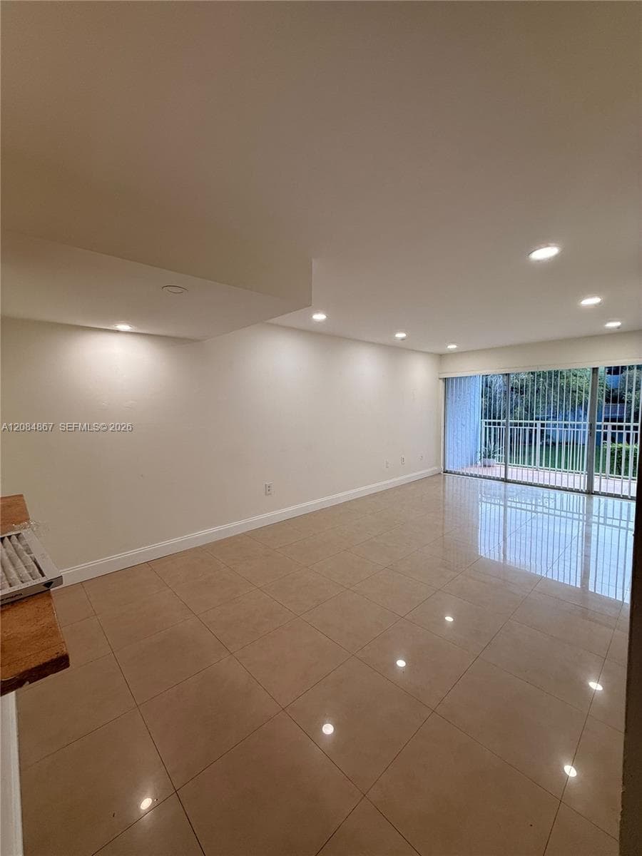 Spacious room featuring polished tile flooring, recessed lighting, and floor-to-ceiling sliding glass doors leading to a private balcony