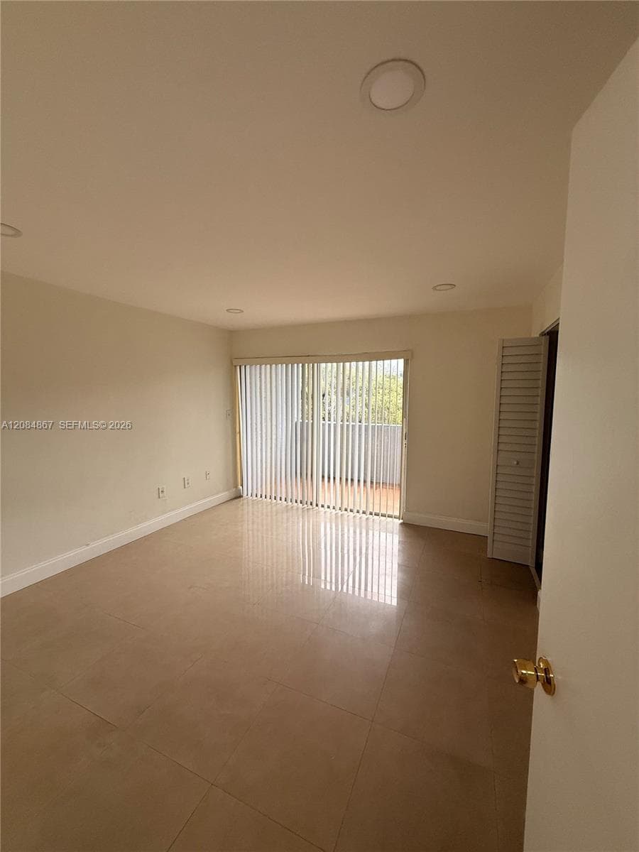 Neutral-toned interior featuring large-format tile flooring, recessed ceiling lighting, and floor-to-ceiling sliding glass doors with vertical blinds