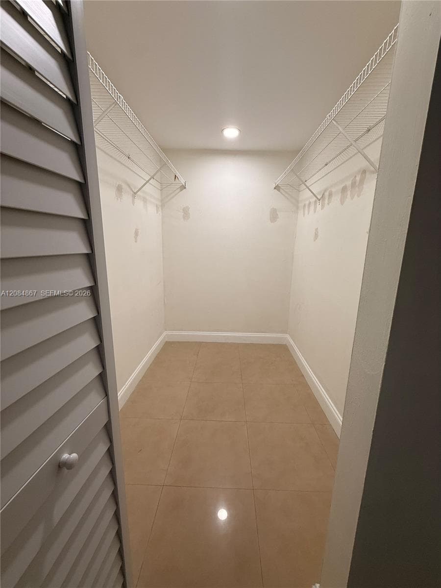 Walk-in closet featuring large-format neutral floor tile, louvered bi-fold doors, and integrated wire shelving