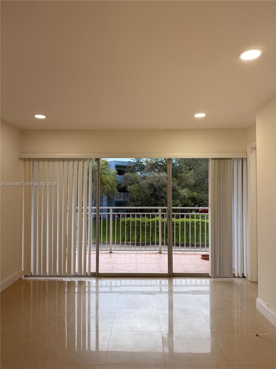 Interior space featuring large-format tile flooring, recessed lighting, and sliding glass doors opening to a private balcony with tiled flooring and metal railing