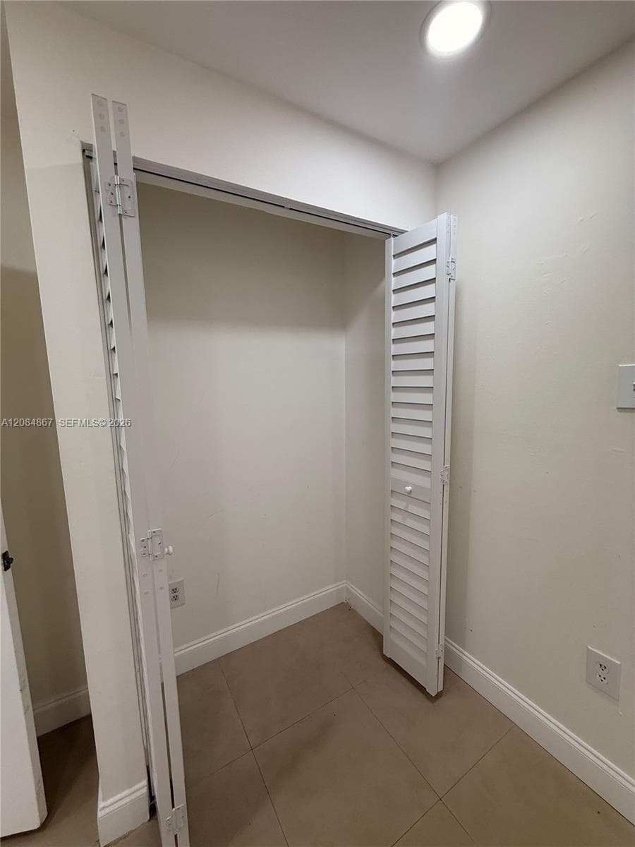 Closet featuring white louvered bifold doors, neutral tile flooring, and integrated recessed ceiling lighting