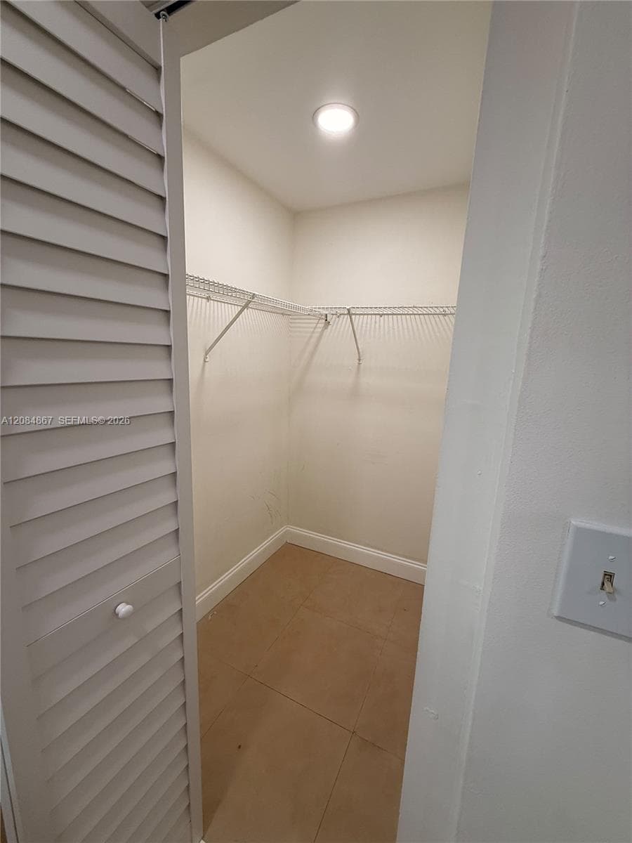 Reach-in closet featuring louvered bi-fold doors, white wire shelving, recessed ceiling lighting, and tile flooring