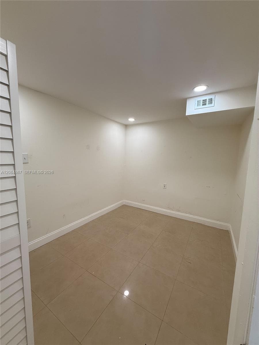 Neutral-toned tile flooring, recessed ceiling lighting, and louvered closet doors