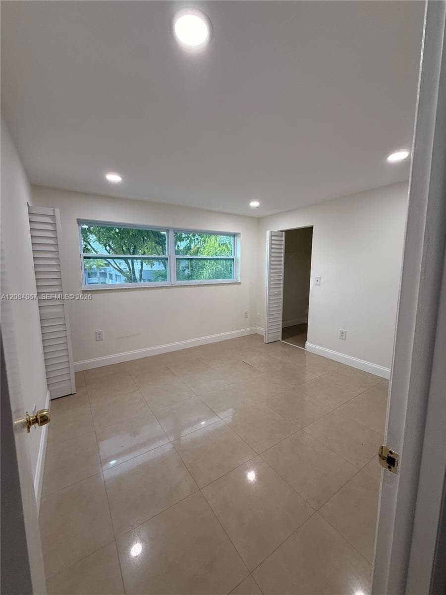 Neutral-toned tile flooring, recessed ceiling lighting, louvered closet doors, and large windows with exterior foliage