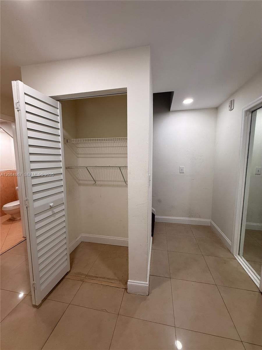 Interior space featuring light-toned tile flooring, louvered closet doors, built-in wire shelving, and recessed ceiling lighting
