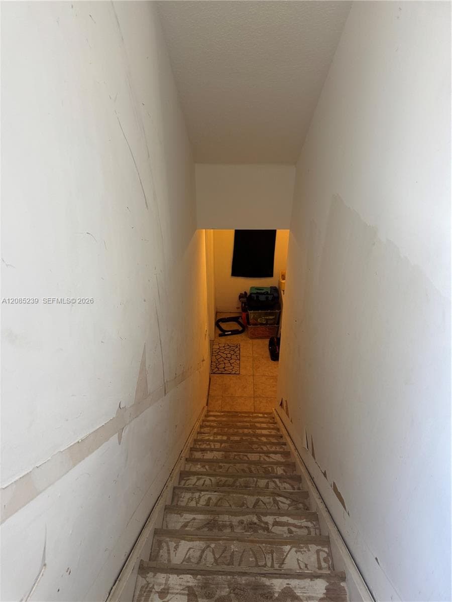 Staircase featuring unfinished treads and drywall surfaces with ceramic tile flooring at the base