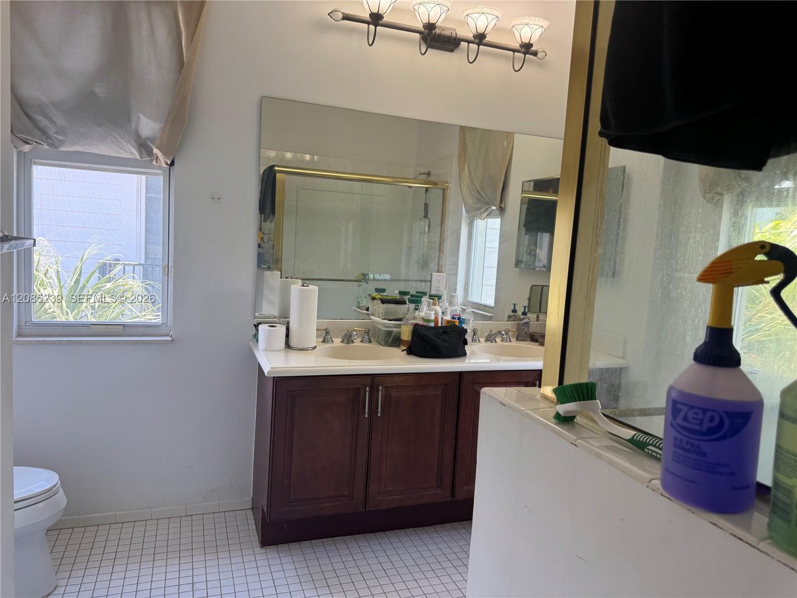 Double-sink vanity featuring dark wood-finish cabinetry, a white countertop, wall-to-wall mirror, and four-bulb overhead vanity lighting