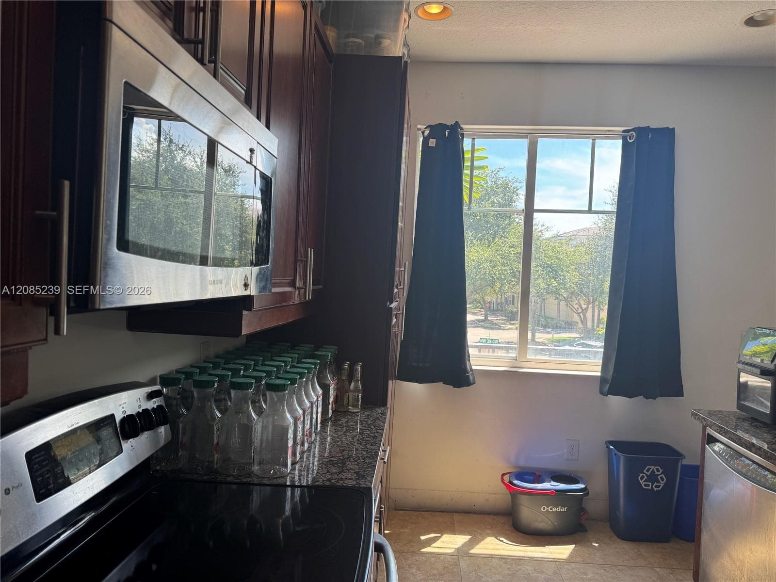 Kitchen featuring dark wood-finish cabinetry, stone-surface countertops, built-in stainless steel microwave, and large window with natural light
