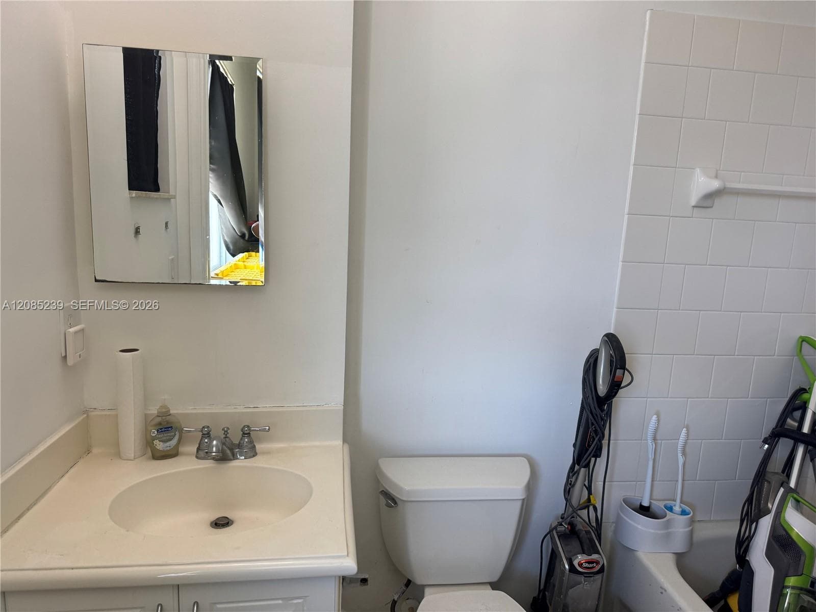 Vanity with integrated sink basin, dual-handle faucet, wall-mounted mirror, and white tile tub surround