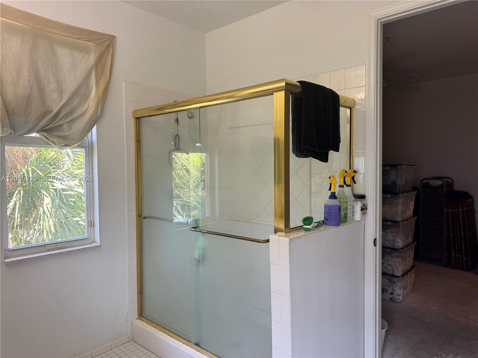 Walk-in shower enclosure with a metallic gold-tone frame, sliding glass doors, and white square wall tiling