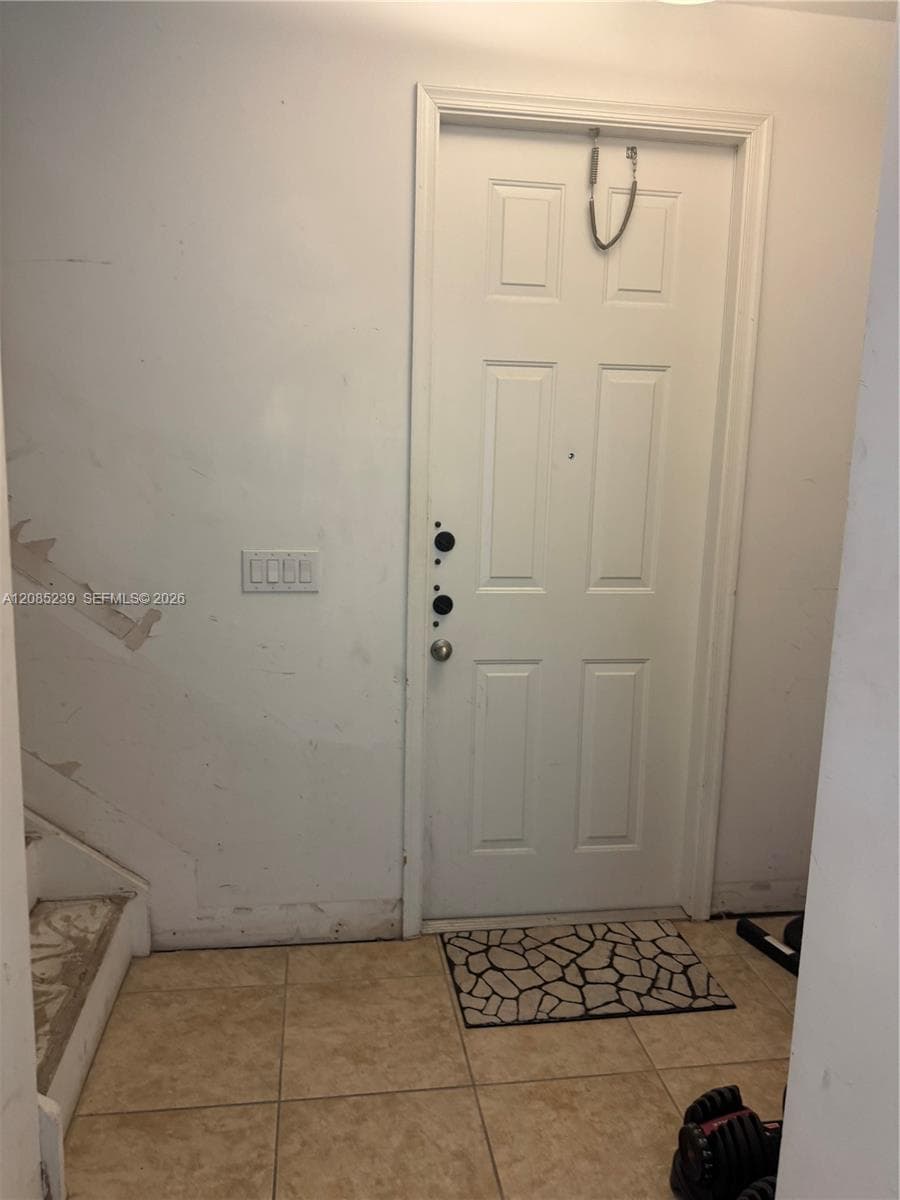 Six-panel entry door with multi-point hardware, ceramic tile flooring, and multi-switch lighting control