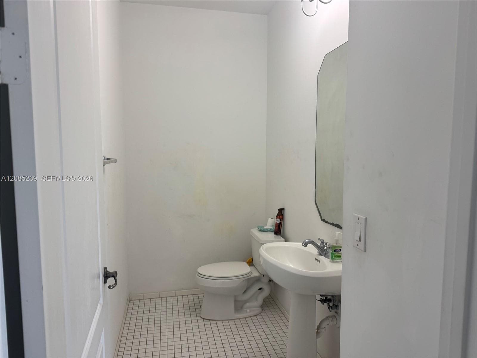 Pedestal sink with chrome faucet, wall-mounted mirror, white ceramic toilet, and tiled flooring
