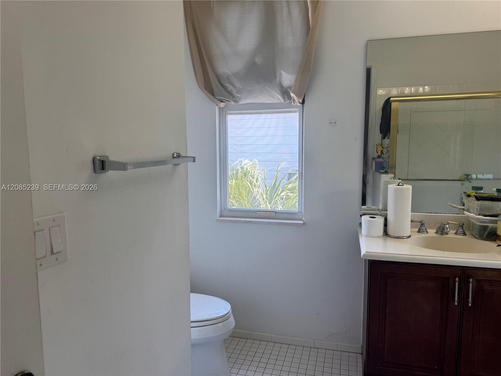 Bathroom featuring a vanity with a white countertop and oval basin, dark wood-finish cabinetry, a large wall-mounted mirror, and tiled flooring