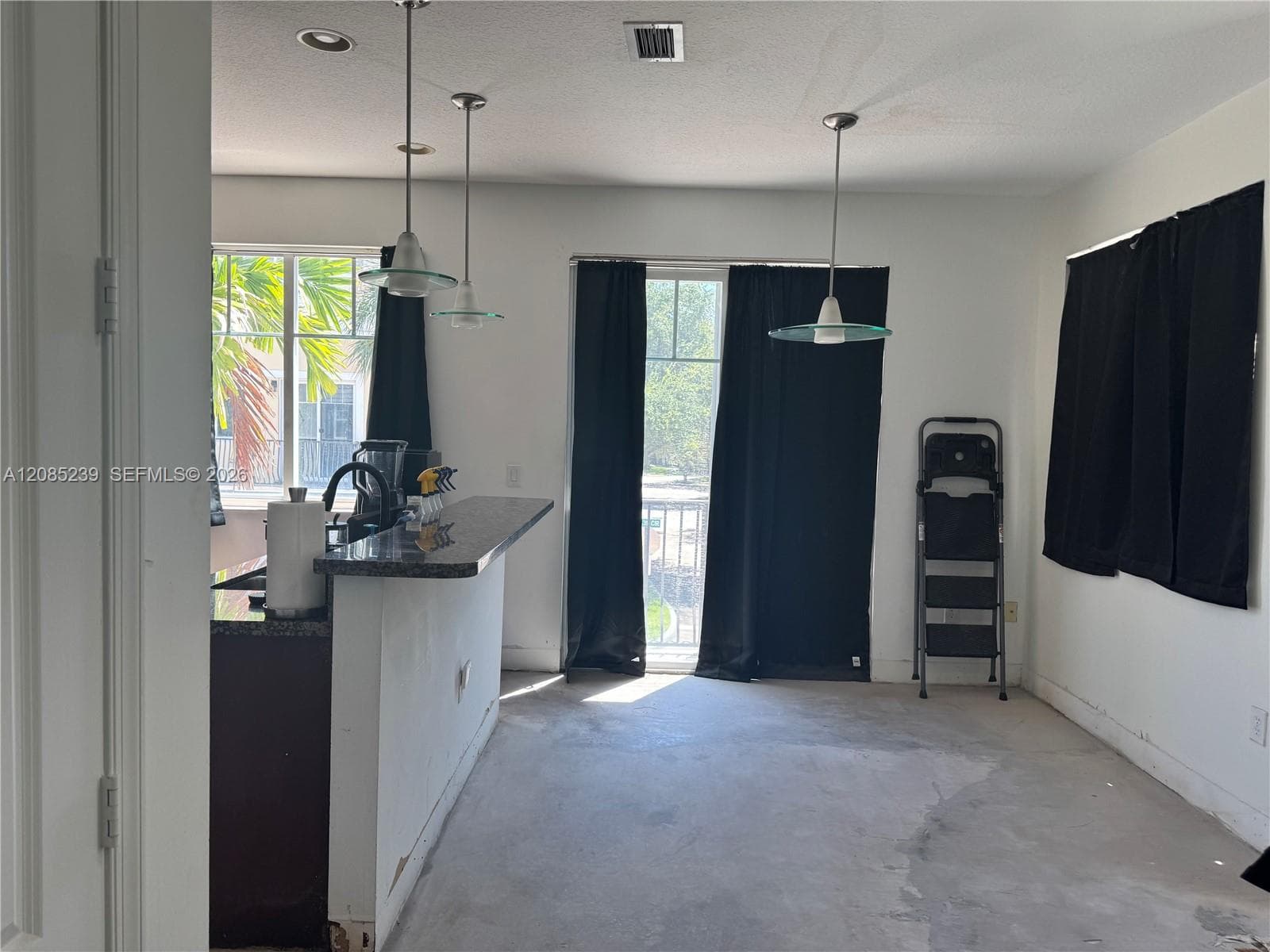 Kitchen area featuring a breakfast bar with stone-finish countertop, three glass-pendant lights, and multiple windows