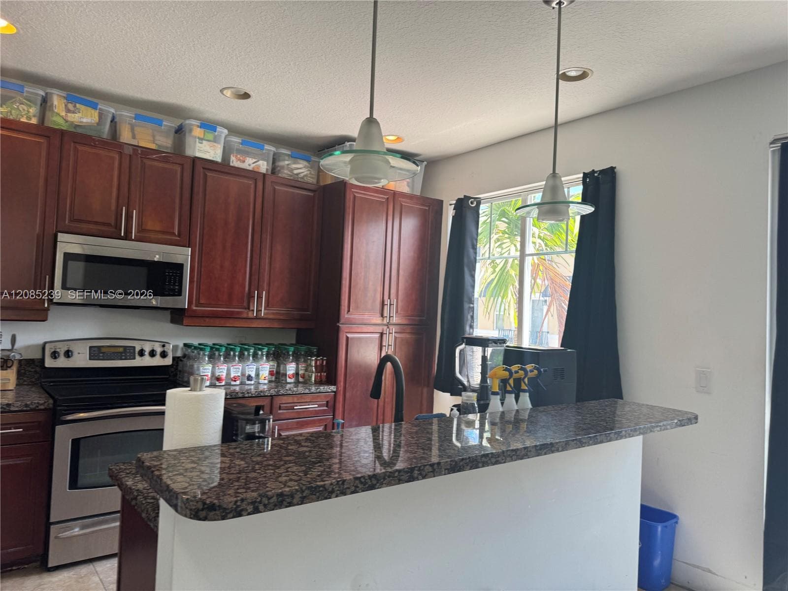 Kitchen featuring wood cabinetry, stone countertops, stainless steel appliances, and dual pendant lighting