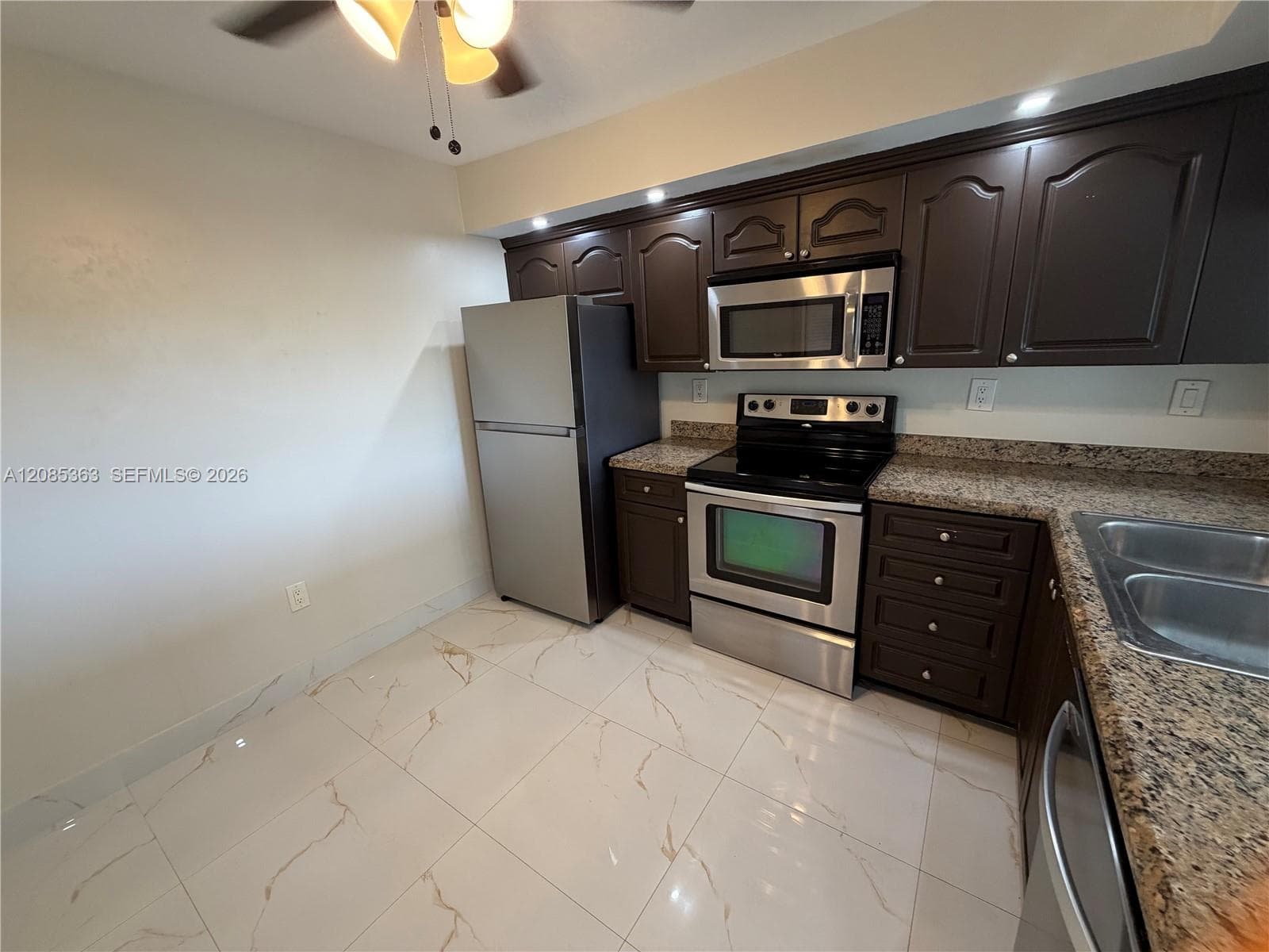 Kitchen featuring dark wood cabinetry, stainless steel appliances, speckled stone-finish countertops, and large-format porcelain tile flooring