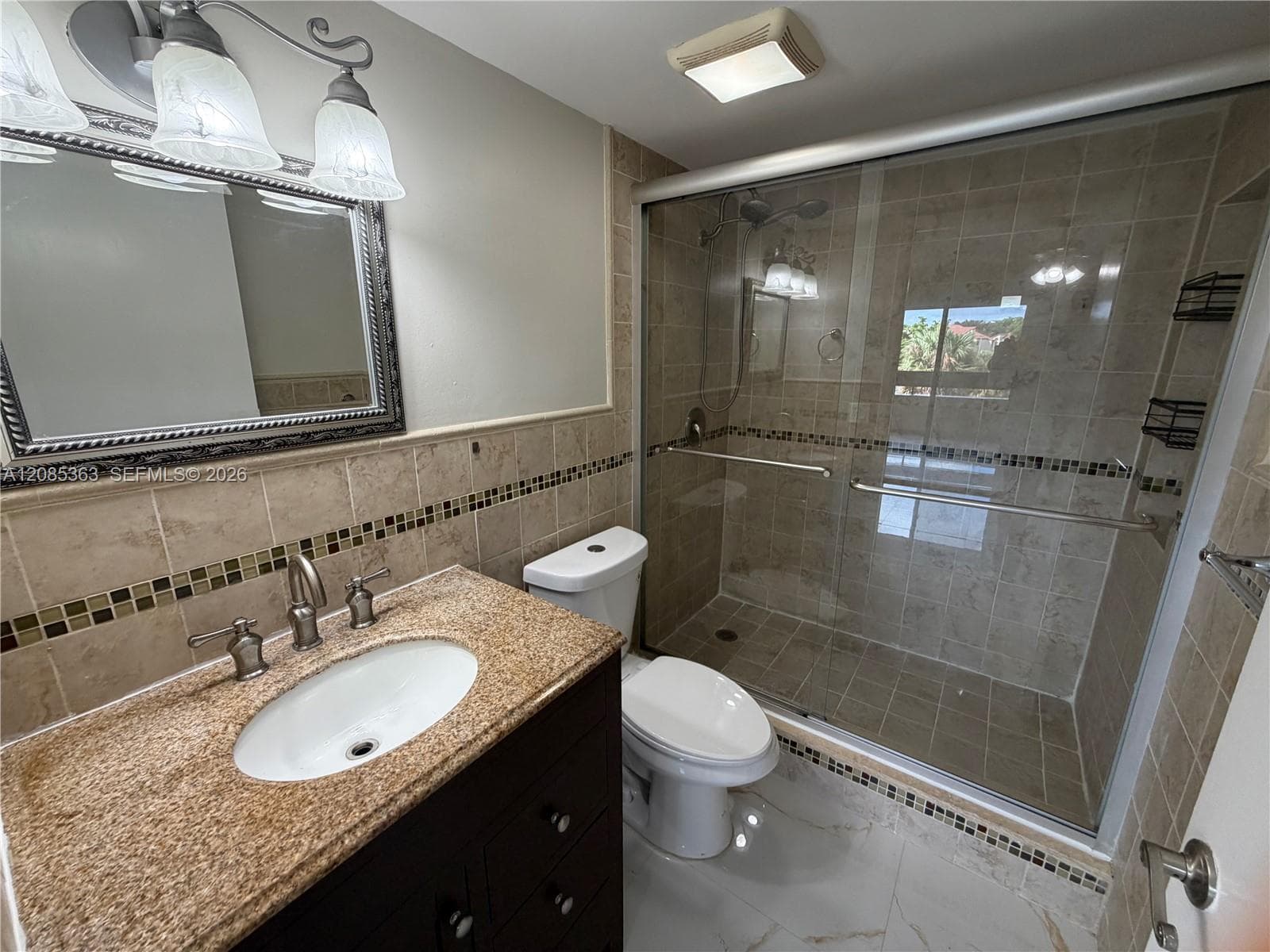 Bathroom featuring a dark wood-finish vanity with a stone countertop, an integrated oval sink, a glass-enclosed shower with tiled surround, and decorative accent tiling