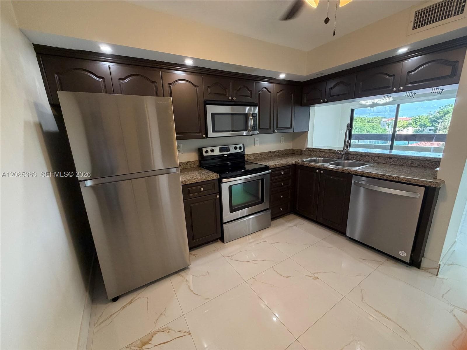 Kitchen featuring dark-finished cabinetry, stainless steel appliances, speckled stone countertops, and polished large-format tile flooring