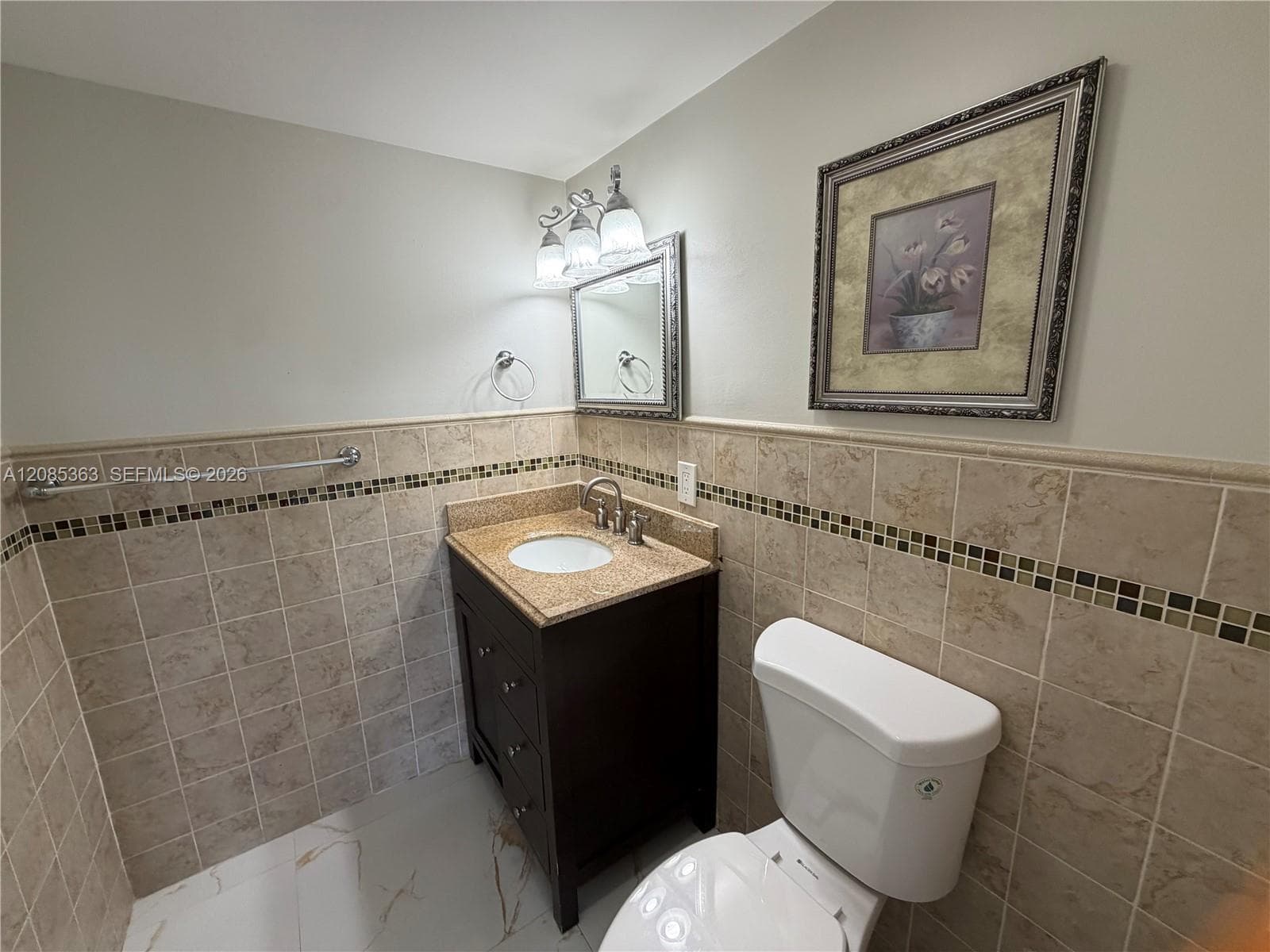 Dark wood vanity with a stone countertop, white ceramic undermount sink, multi-tone tiled wall backsplash, and three-light wall-mounted fixture