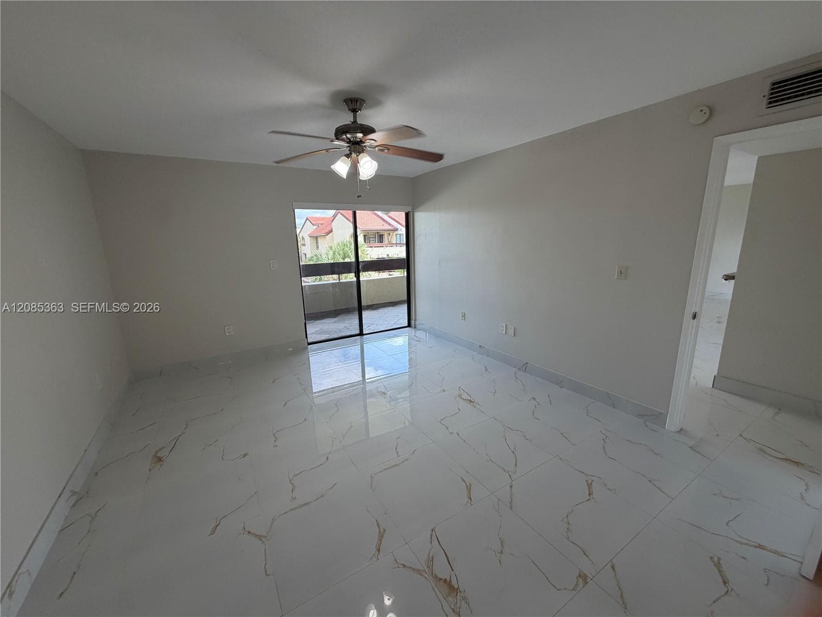 Large-format tile flooring with a neutral veined finish, ceiling fan with integrated lighting, and sliding glass door with access to a private balcony