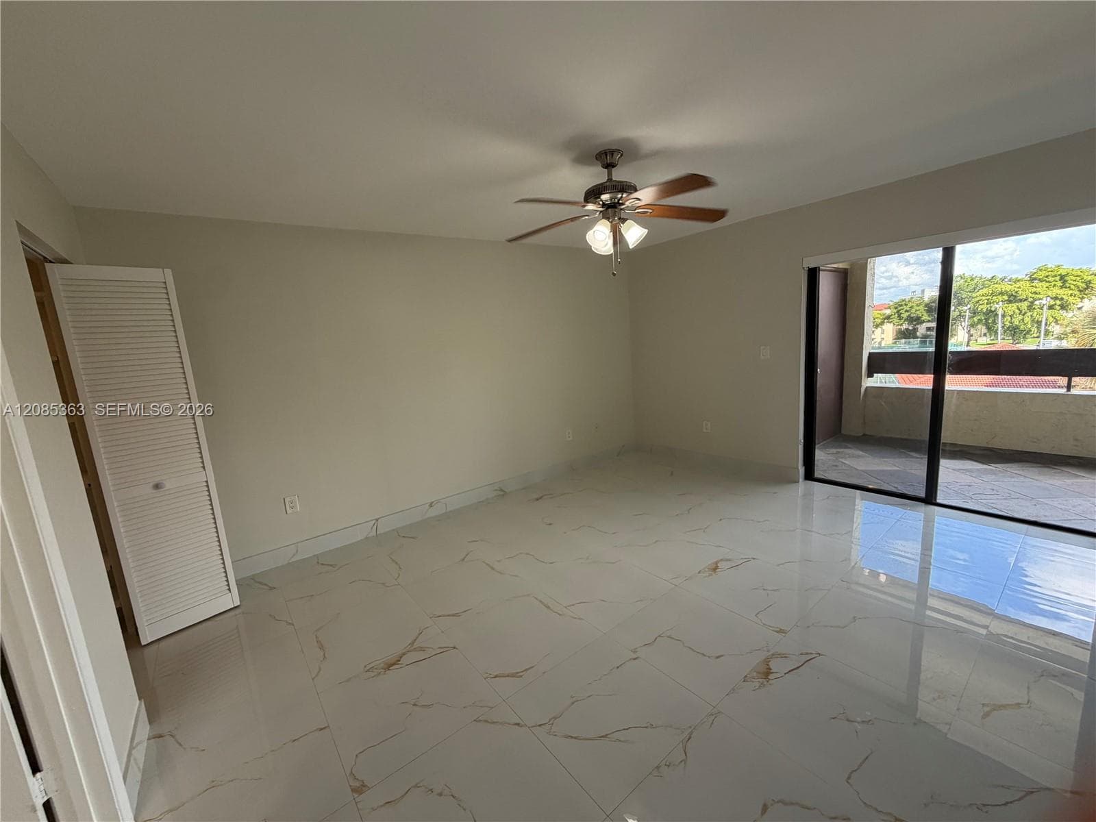 Large format stone-finish tile flooring, ceiling fan with integrated lighting, bifold closet doors, and floor-to-ceiling glass sliding doors opening to an exterior balcony