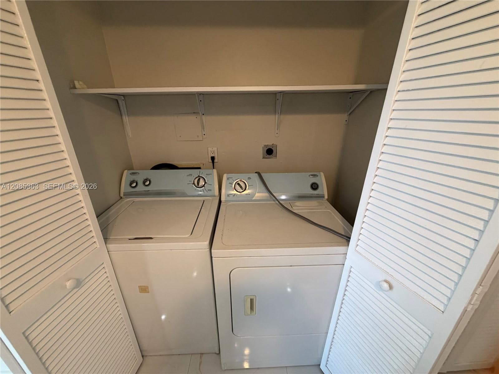 Laundry closet featuring louvered bifold doors and an integrated overhead storage shelf
